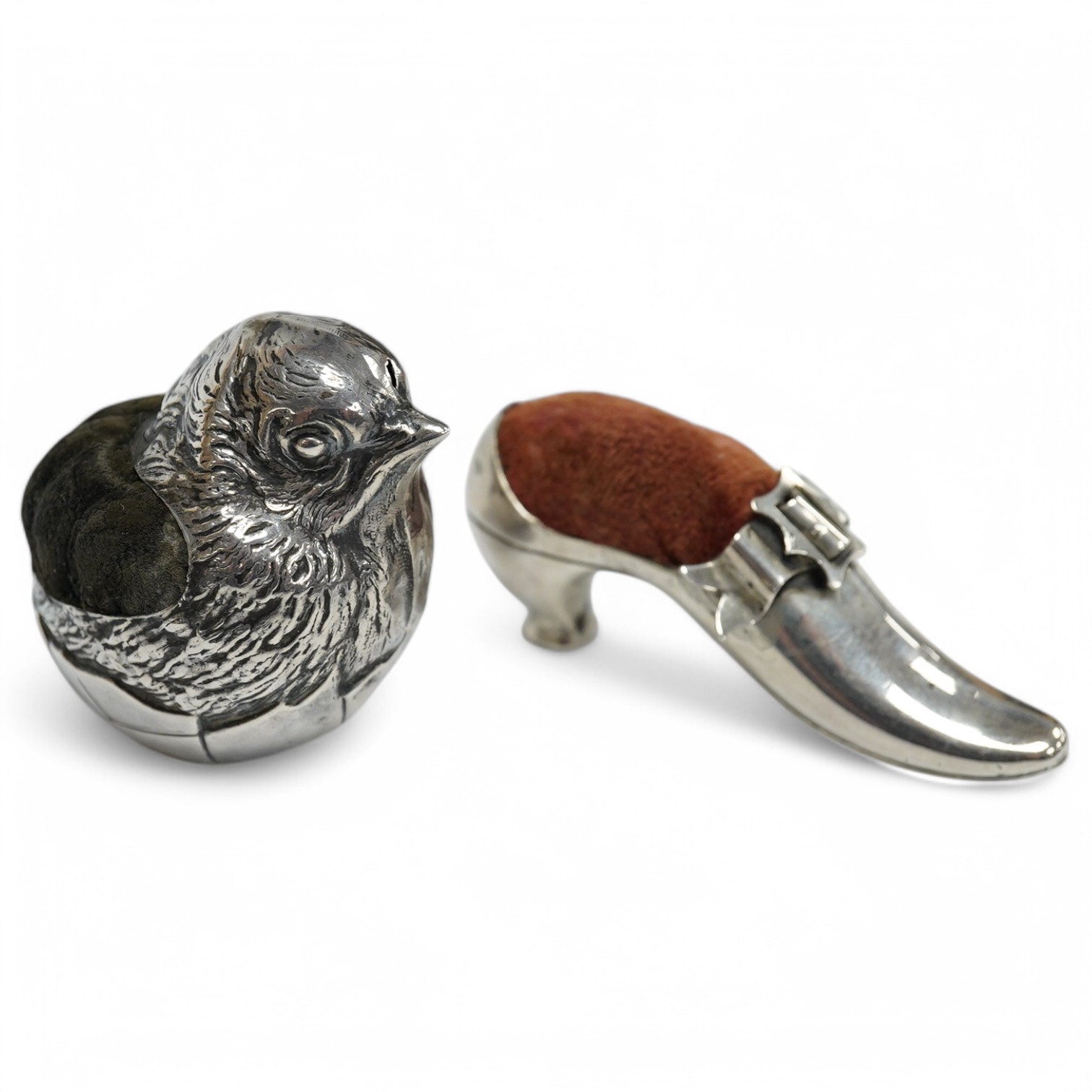 An Edwardian novelty silver pin cushion, modelled as a hatching chick, by Sampson Mordan & Co, Sheffield, 1906, height 43mm (hole), together with a late Victorian shoe pin cushion, by Adie & Lovekin, Birmingham, 1892, Co